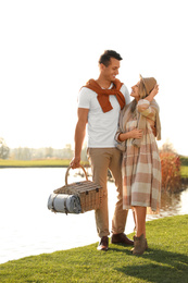 Photo of Young couple with picnic basket near lake on sunny day