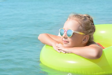 Photo of Little girl with inflatable ring in sea on sunny day, space for text