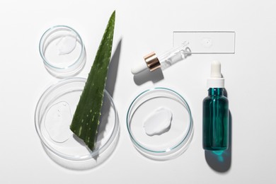 Bottle of cosmetic serum, aloe vera leaf and petri dishes with samples on white background, flat lay