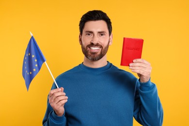 Photo of Immigration. Happy man with passport and flag of European Union on orange background