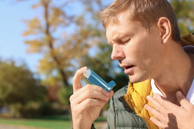 Photo of Man using asthma inhaler outdoors. Space for text