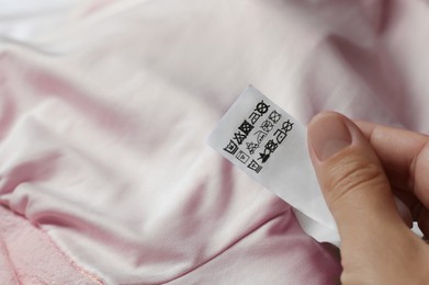 Woman holding clothing label on beige garment, closeup