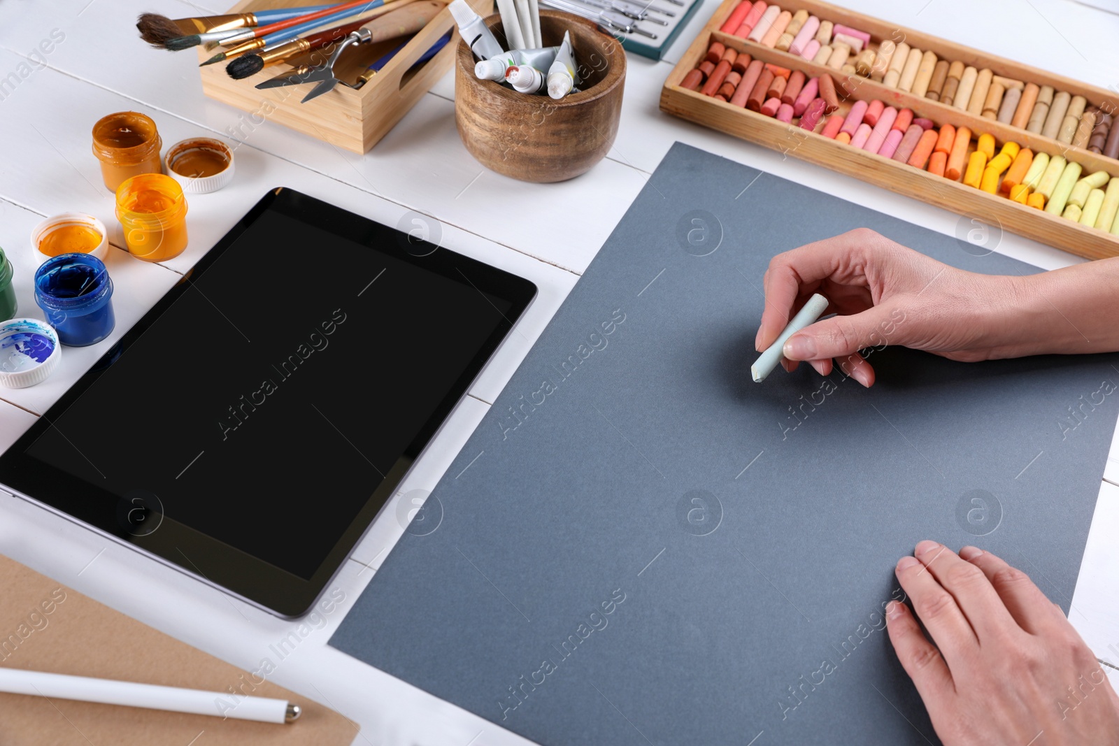 Photo of Artist drawing with chalk pastel on grey paper at white wooden table, closeup