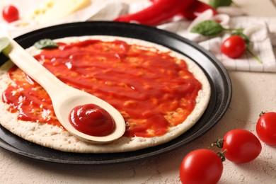 Photo of Pizza base smeared with sauce and tomatoes on light textured table, closeup