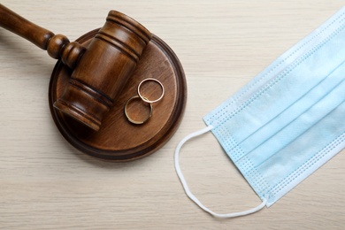 Photo of Gavel, protective mask and wedding rings on wooden table, flat lay. Divorce during coronavirus quarantine