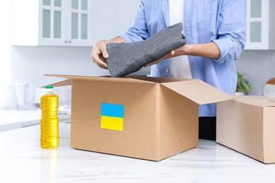 Photo of Humanitarian aid for Ukraine. Man putting clothes in donation box at white table indoors, closeup