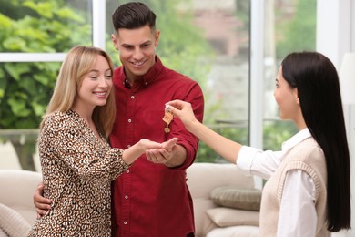 Real estate agent giving house key to couple indoors