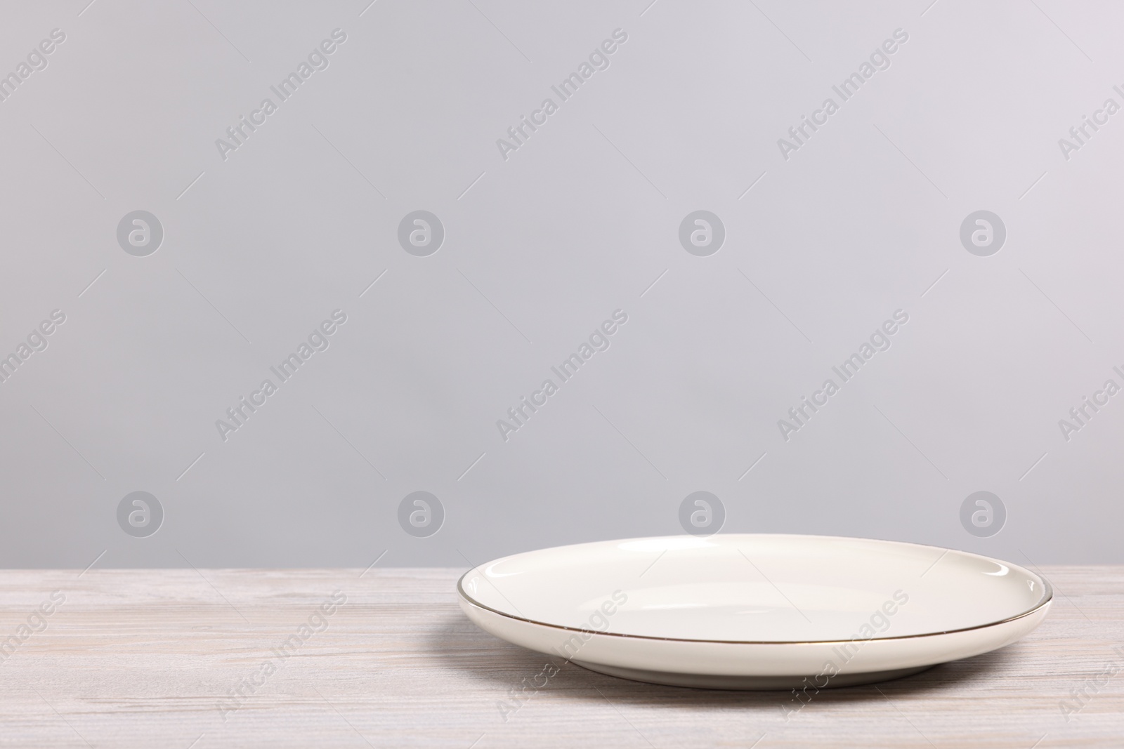 Photo of Empty ceramic plate on wooden table against light background, space for text