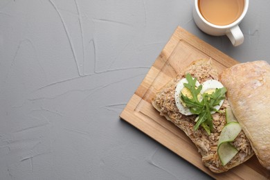 Delicious sandwich with tuna, boiled egg, vegetables and cup of tea on light grey table, flat lay. Space for text