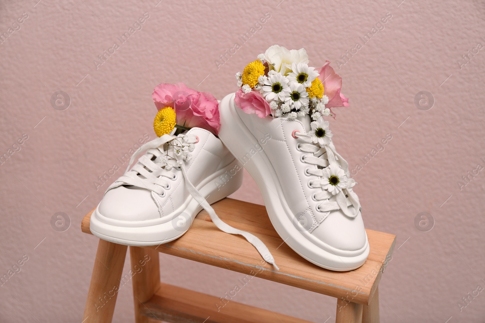 Photo of Shoes with beautiful flowers on wooden stand against pale pink background