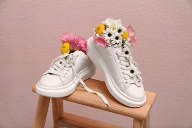Photo of Shoes with beautiful flowers on wooden stand against pale pink background