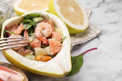 Photo of Delicious pomelo salad with shrimps in half of fruit on white marble table, closeup. Space for text