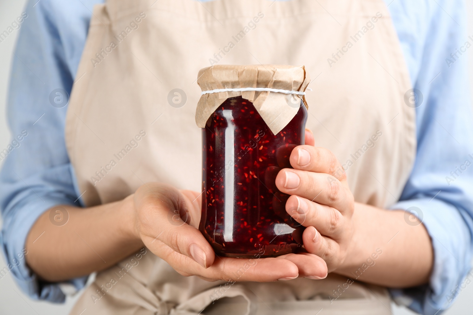 Photo of Woman holding glass jar of raspberry jam, closeup