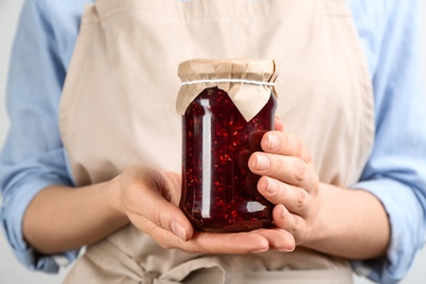 Photo of Woman holding glass jar of raspberry jam, closeup