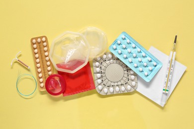 Contraceptive pills, condoms, intrauterine device and thermometer on yellow background, flat lay. Different birth control methods
