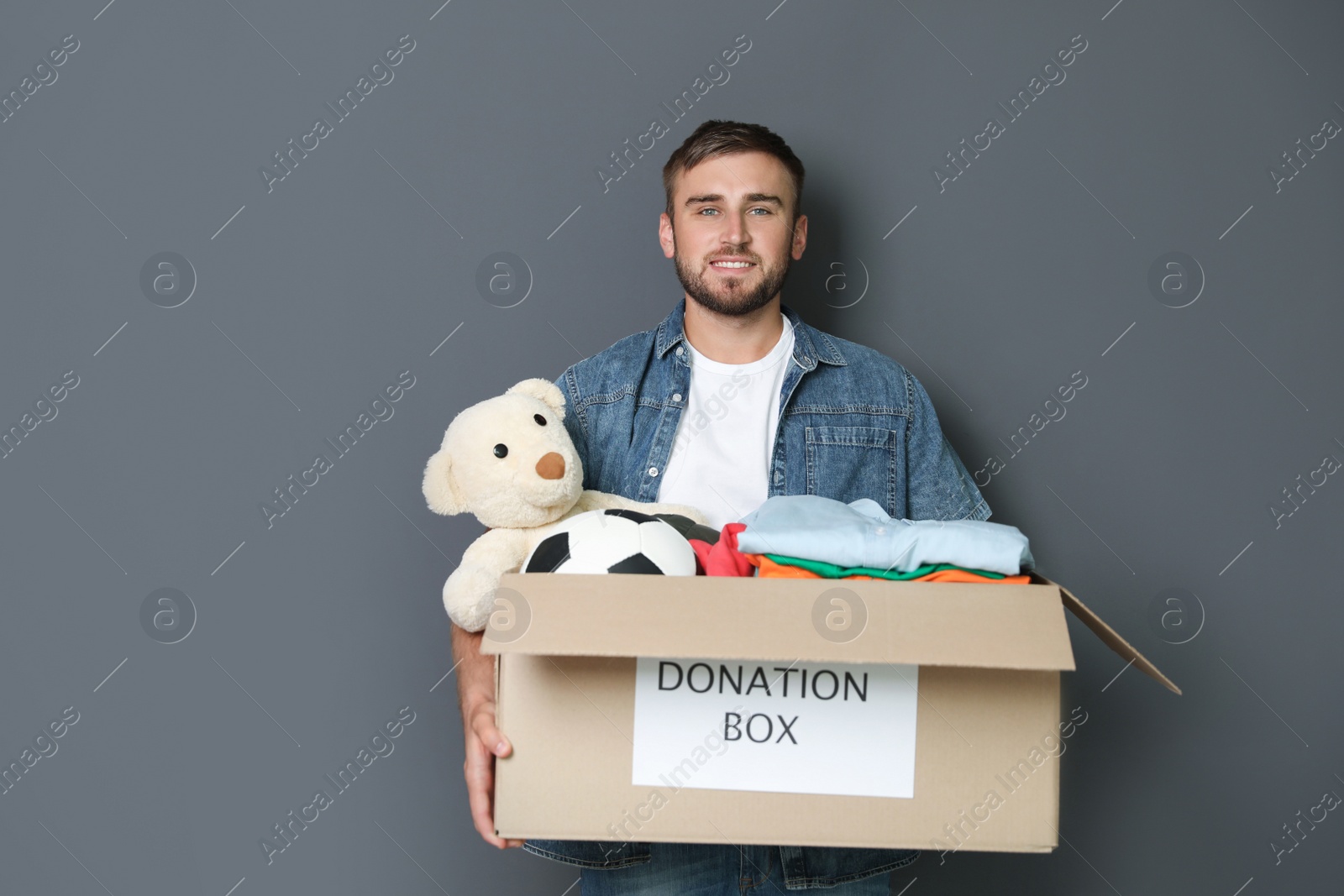 Photo of Young man holding box with donations on grey background