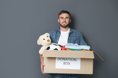 Young man holding box with donations on grey background