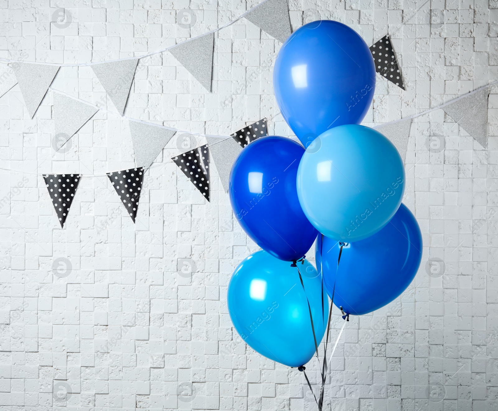 Photo of Blue balloons near white wall decorated with flag garlands. Greeting card