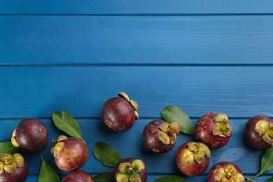 Delicious tropical mangosteens on blue wooden table, flat lay. Space for text