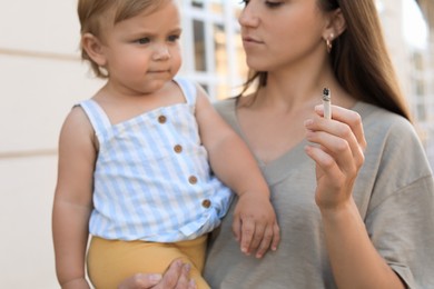 Mother with cigarette and child outdoors, focus on hand. Don't smoke near kids