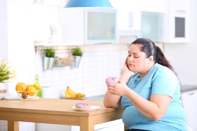 Sad overweight woman with donuts in kitchen. Failed diet