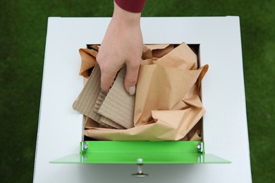 Woman putting cardboard into trash bin on color background, closeup. Recycling concept