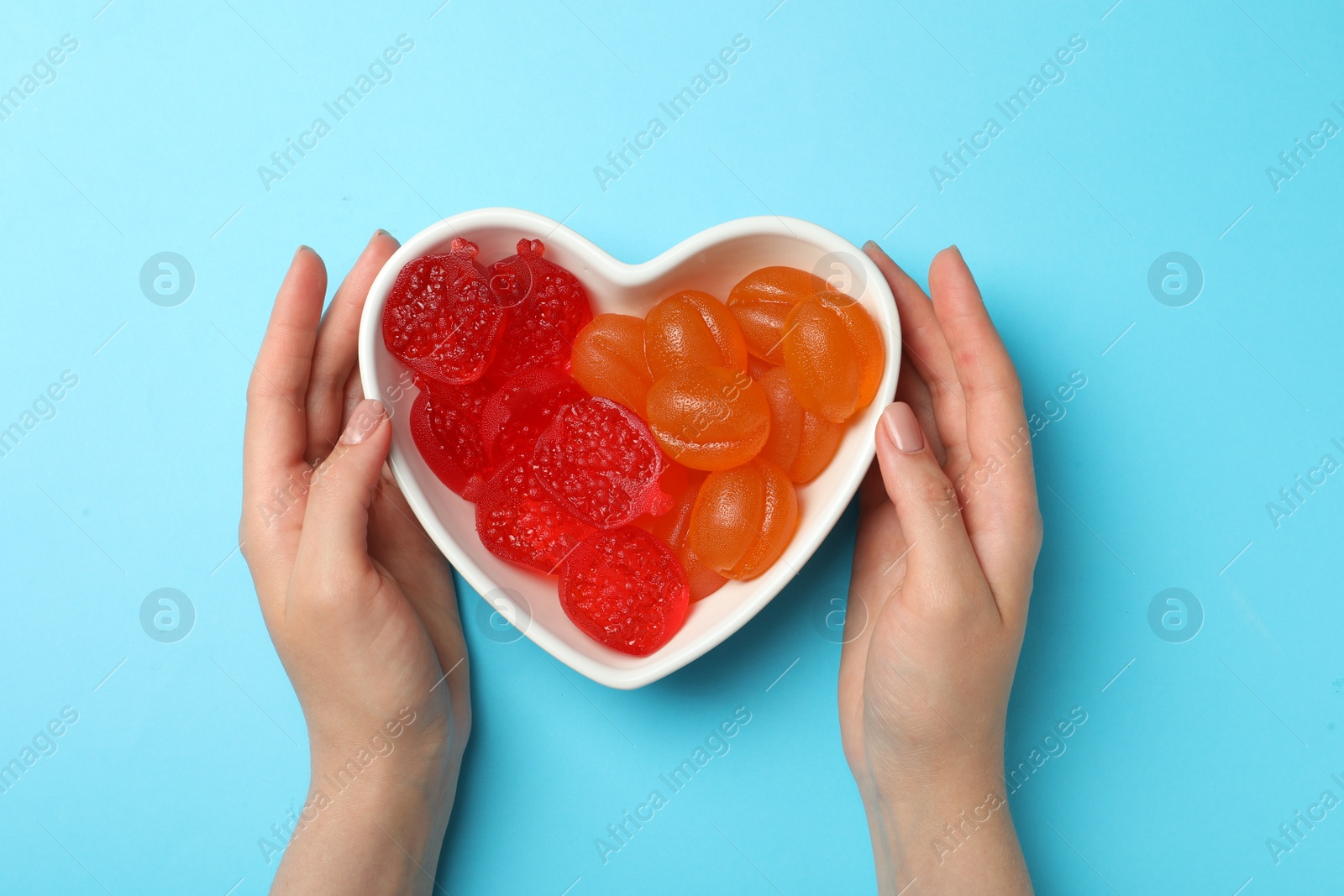 Photo of Woman with delicious gummy candies on light blue background, top view