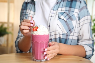 Photo of Woman holding tasty fresh milk shake with strawberry at table indoors, closeup