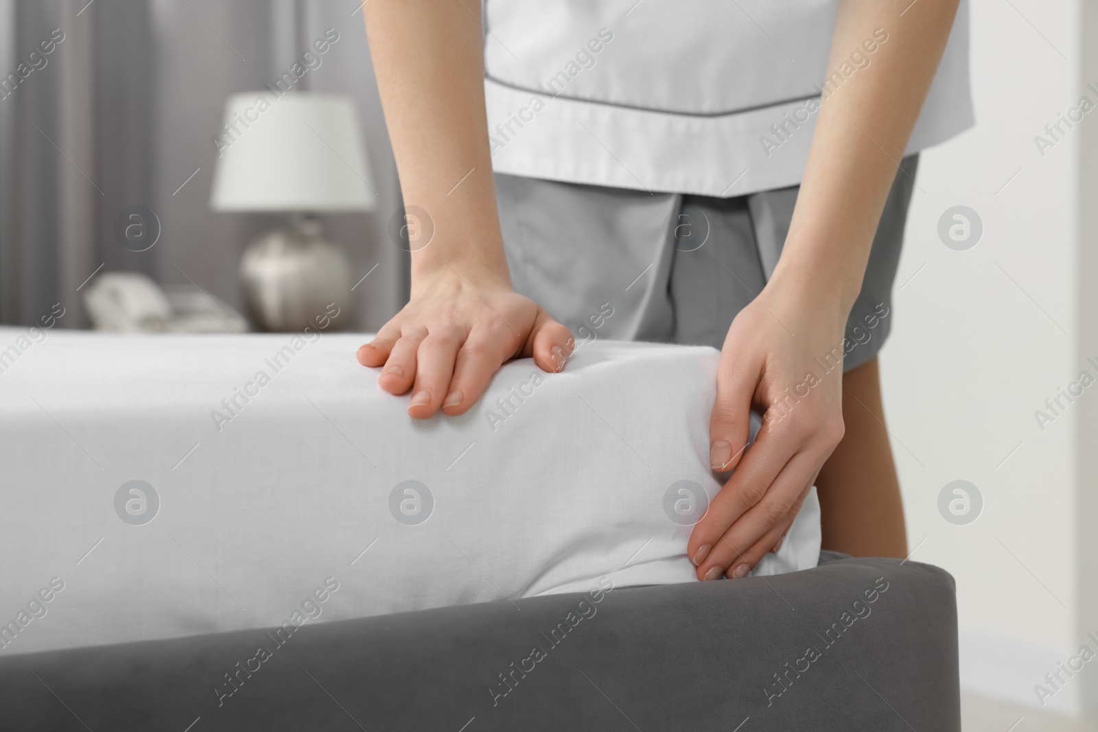 Photo of Young maid making bed in hotel room, closeup