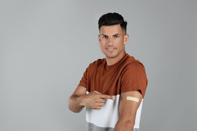 Photo of Vaccinated man showing medical plaster on his arm against grey background