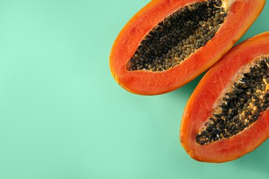 Photo of Halves of fresh ripe papaya on light turquoise background, flat lay with space for text. Exotic fruit