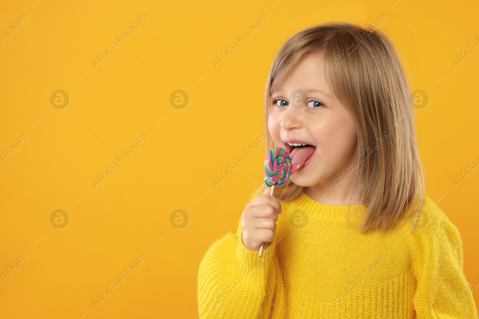 Photo of Portrait of cute girl licking lollipop on orange background, space for text