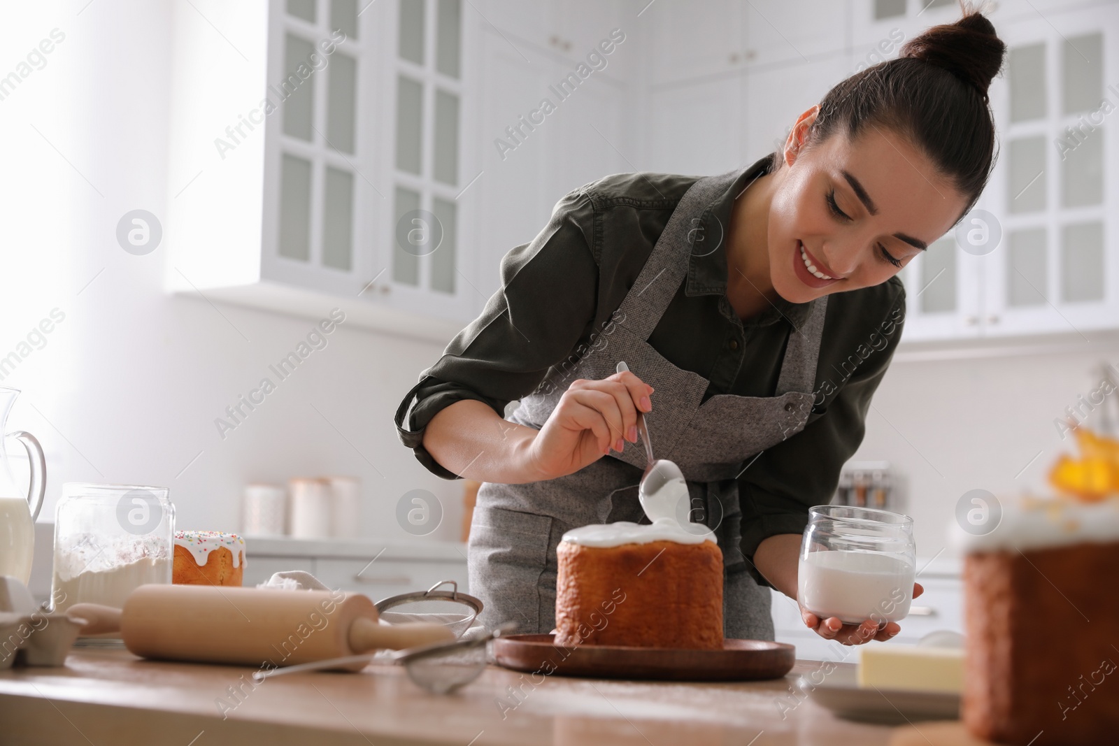 Photo of Young woman decorating traditional Easter cake with glaze in kitchen. Space for text