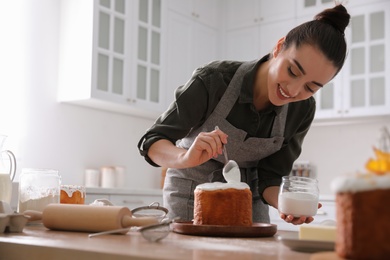 Young woman decorating traditional Easter cake with glaze in kitchen. Space for text