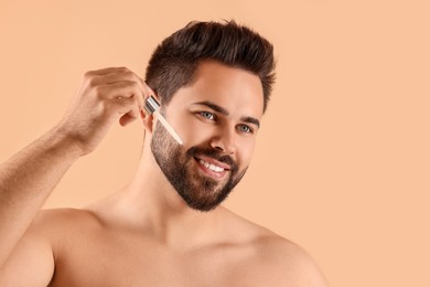 Photo of Handsome man applying cosmetic serum onto face on beige background, space for text