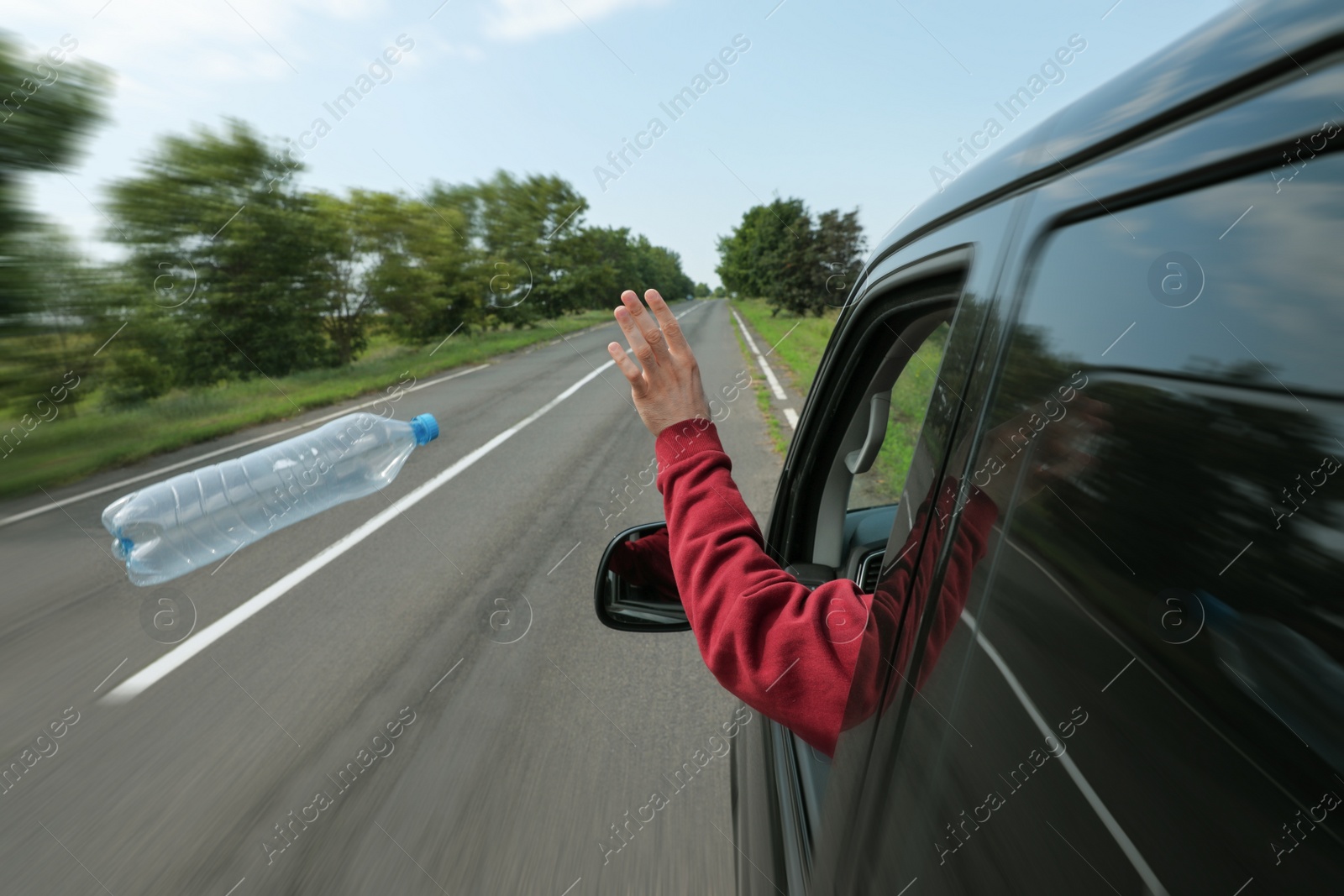 Photo of Driver throwing away plastic bottle from car window. Garbage on road