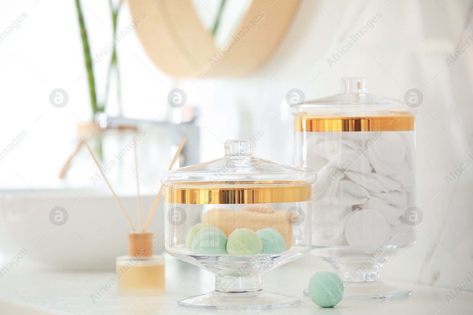 Photo of Jars with cotton pads and bath bombs on white countertop in bathroom