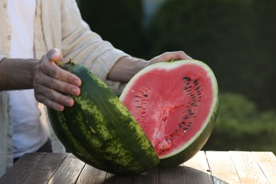 Photo of Man with tasty ripe watermelon at wooden table outdoors, closeup