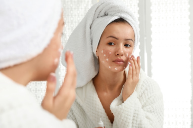 Photo of Teen girl with acne problem applying cream near mirror in bathroom