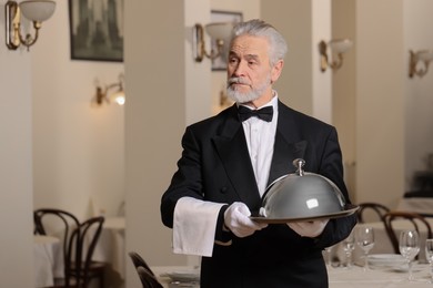 Photo of Butler holding metal tray with lid in restaurant. Space for text