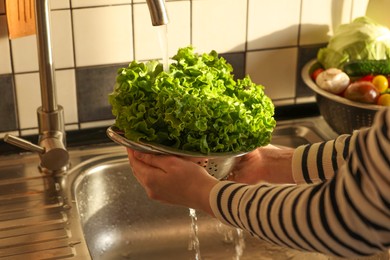 Photo of Woman washing fresh lettuce leaves in metal colander, closeup