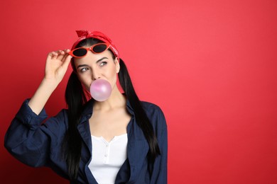 Photo of Fashionable young woman in pin up outfit blowing bubblegum on red background, space for text