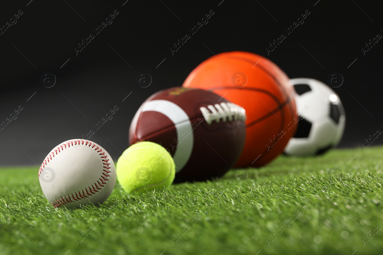 Photo of Many different sports balls on green grass against black background, closeup