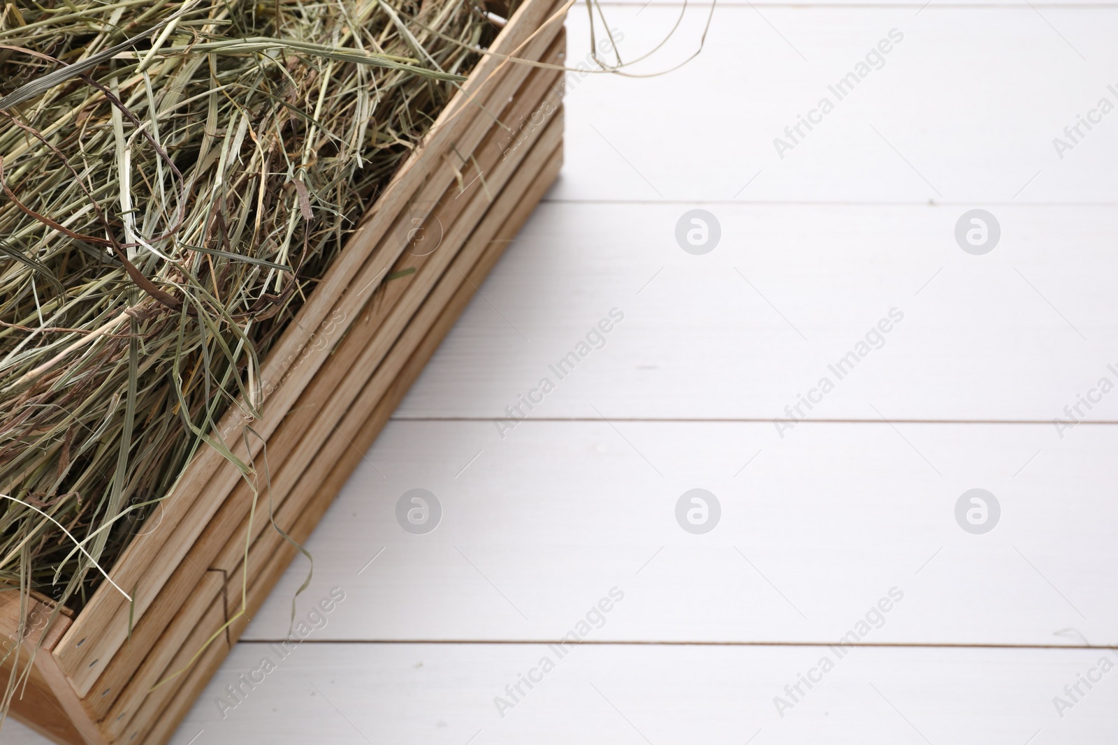 Photo of Crate with dried hay on white wooden table, closeup. Space for text