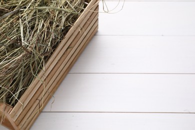 Crate with dried hay on white wooden table, closeup. Space for text