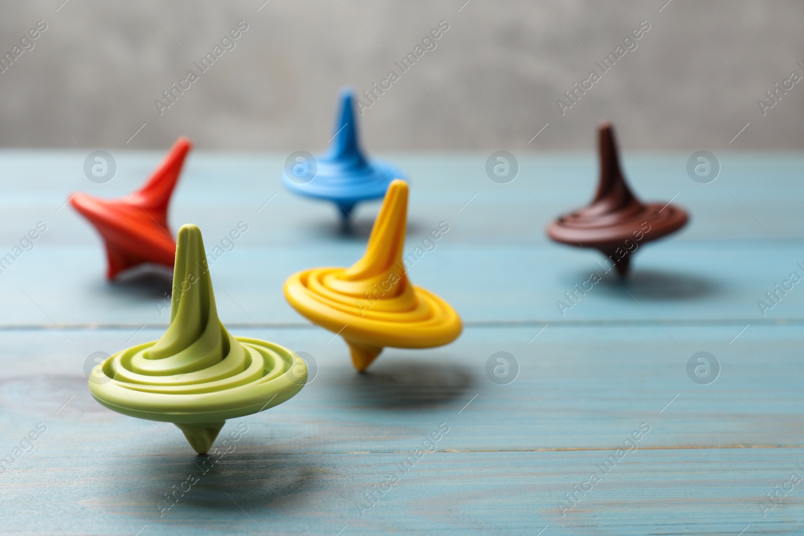 Photo of Bright spinning tops on light blue wooden table, closeup