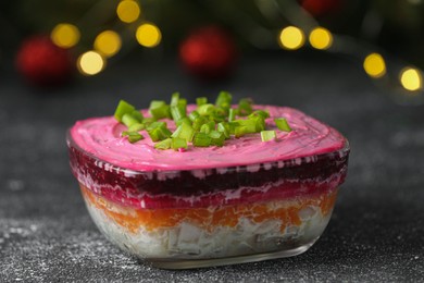 Photo of Herring under fur coat salad on grey table against blurred festive lights, closeup. Traditional Russian dish