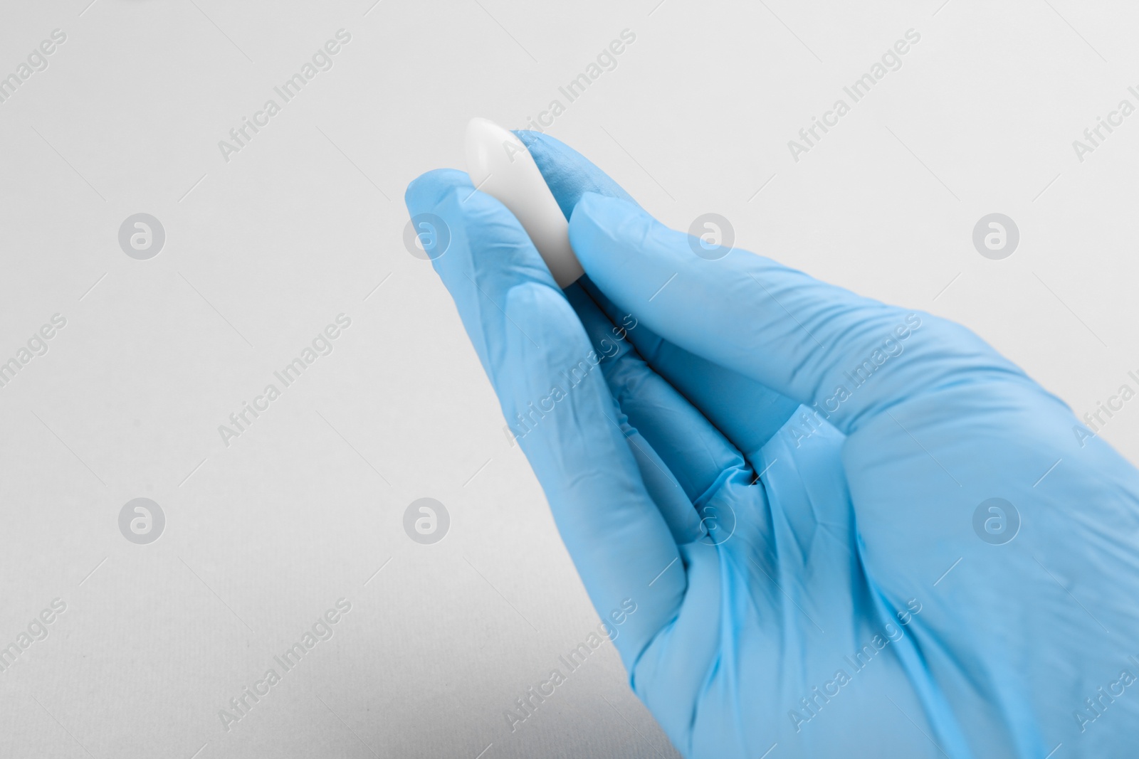 Photo of Woman holding suppository on light background, closeup. Hemorrhoid treatment