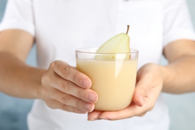 Photo of Woman holding tasty pear juice on light blue background, closeup