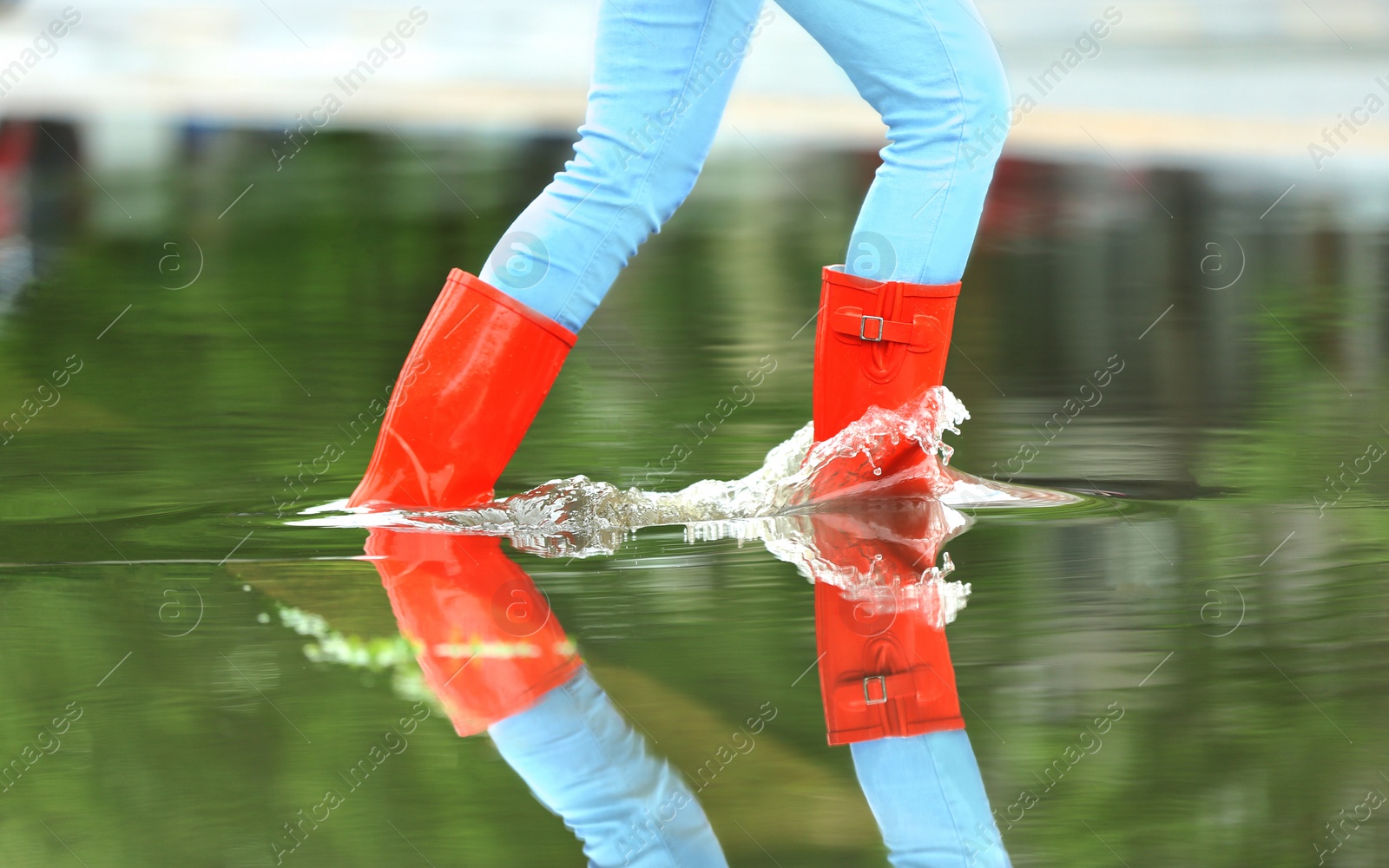 Photo of Woman with red rubber boots running in puddle, closeup. Rainy weather